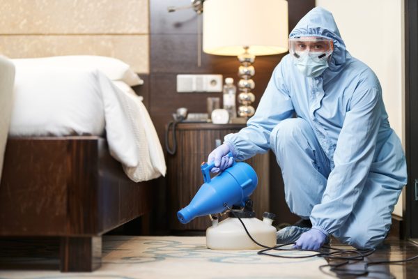 Worker in biohazard suit and mask disinfecting bedroom Worker in biohazard suit and mask disinfecting bedroom